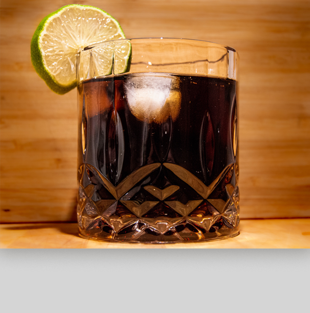 Billede med cola i et glas med isterninger og lime på glaskanten, skal ligne rom og cola